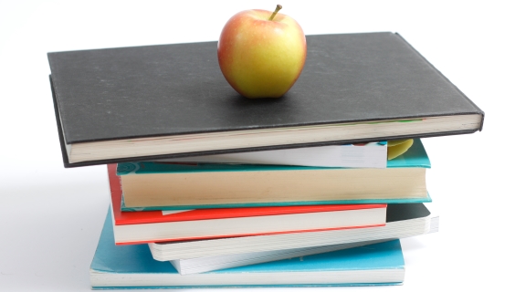 En stak bøger med et gult og rødt æble på toppen